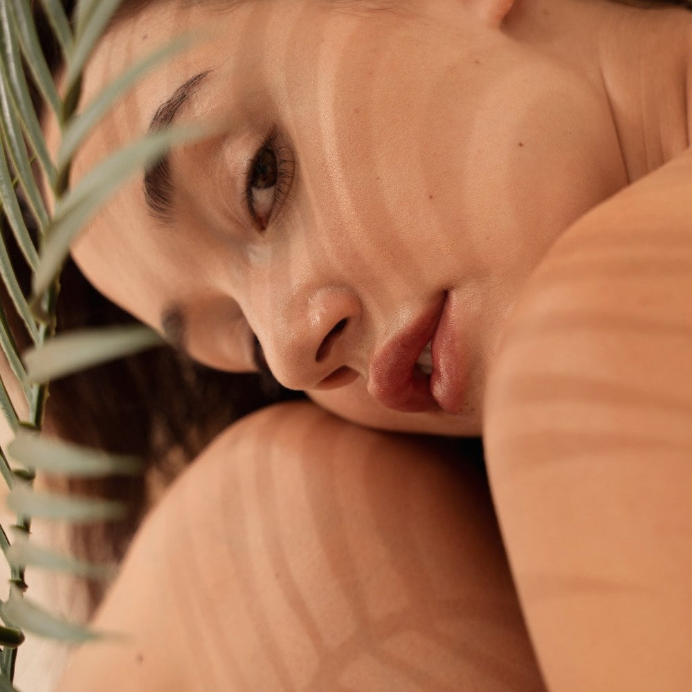 Woman with head laying on her knees behind palm leaf